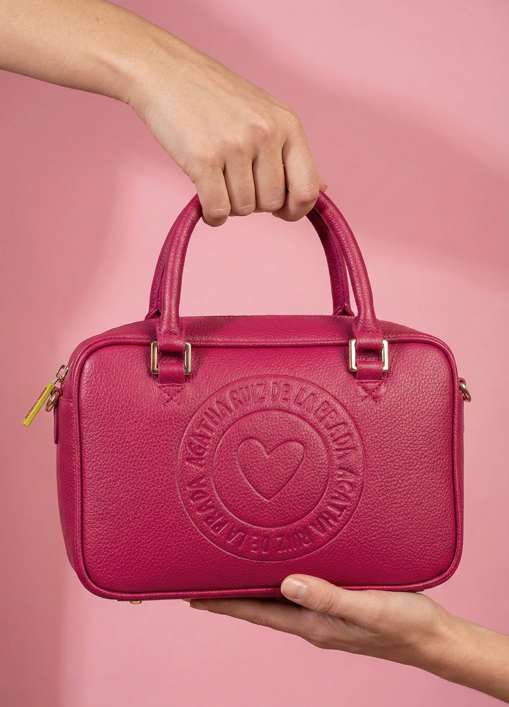 Detalle del logo circular grabado con corazón central. Mini bolso fucsia con formato rectangular y logo frontal.